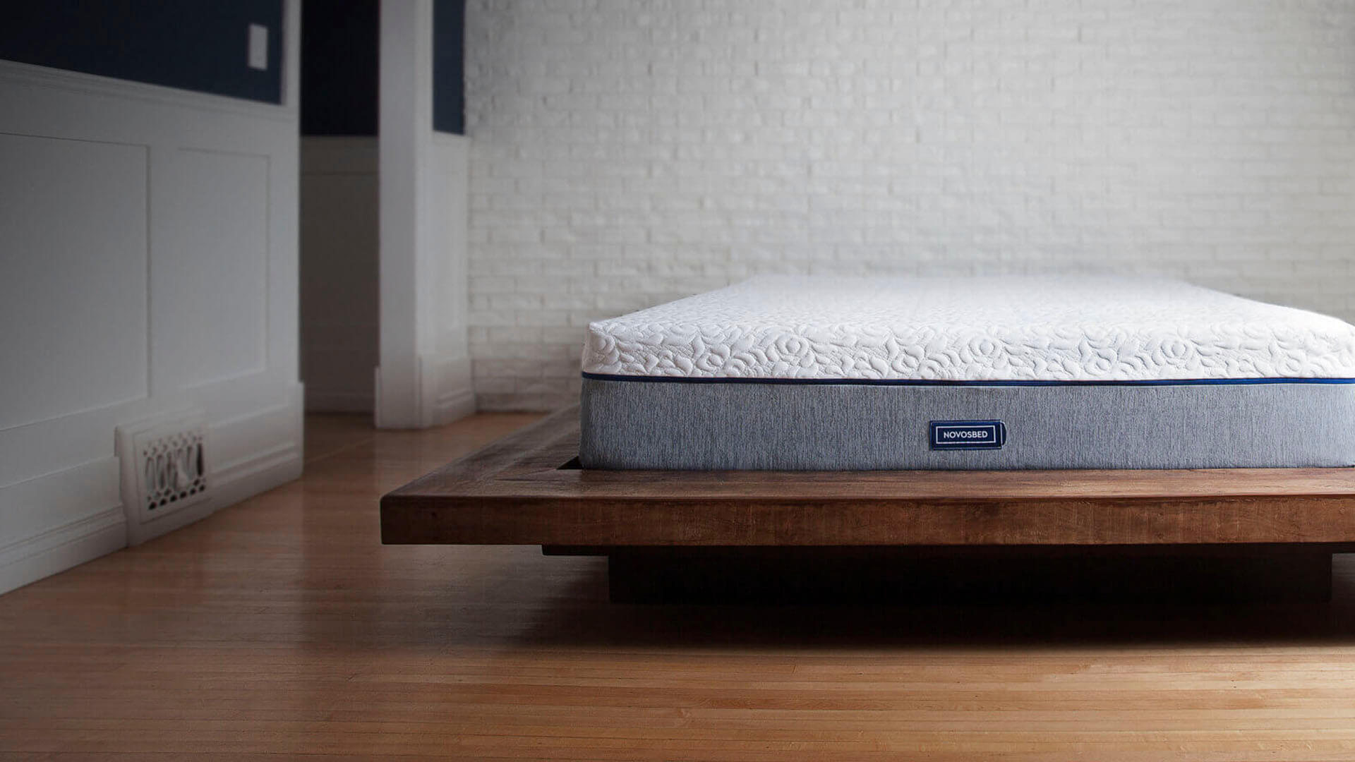 Image of a Novosbed premium memory foam mattress resting on a brown platform bed frame in a stylish white brick bedroom.