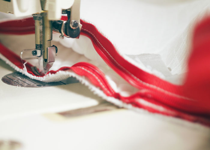 Image of the red zipper being sewn onto the white Douglas mattress cover with a sewing machine.