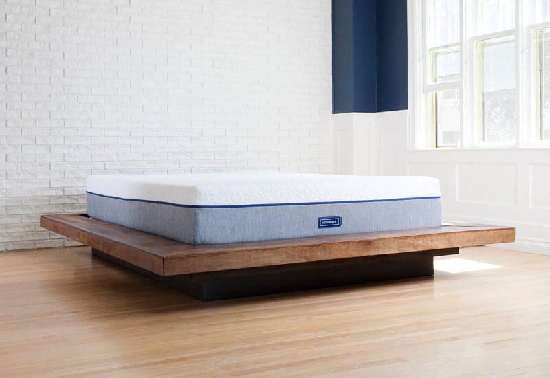 Image of a Novosbed premium memory foam mattress resting on a brown platform bed frame in a sunny bedroom.