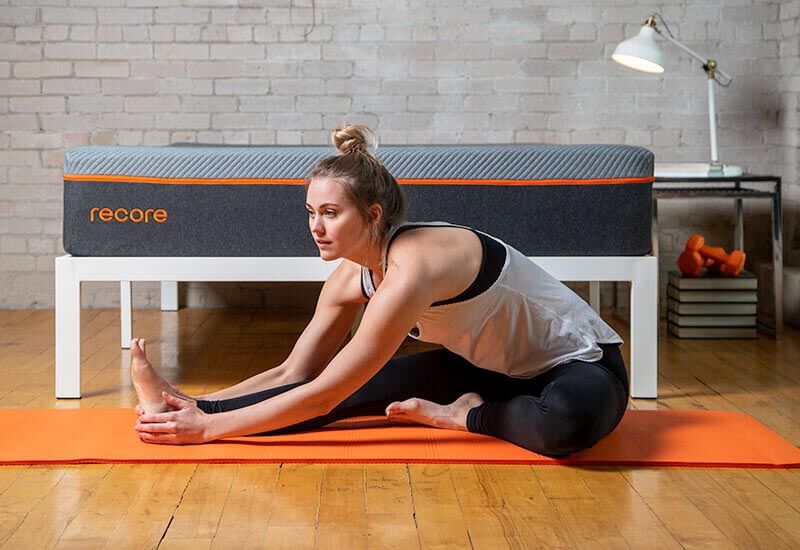 Image of a young female doing yoga stretches in front of the Recore performance latex mattress.