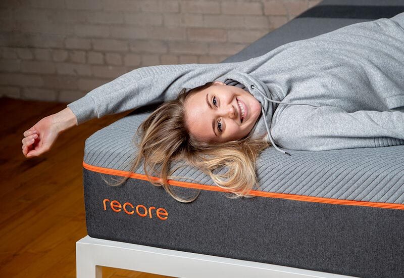 Image of a smiling young woman in athletic clothes lying atop the Recore performance latex mattress.