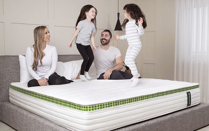 Image of a family on the Brunswick hybrid spring and foam mattress with the parents smiling and children jumping up and down.
