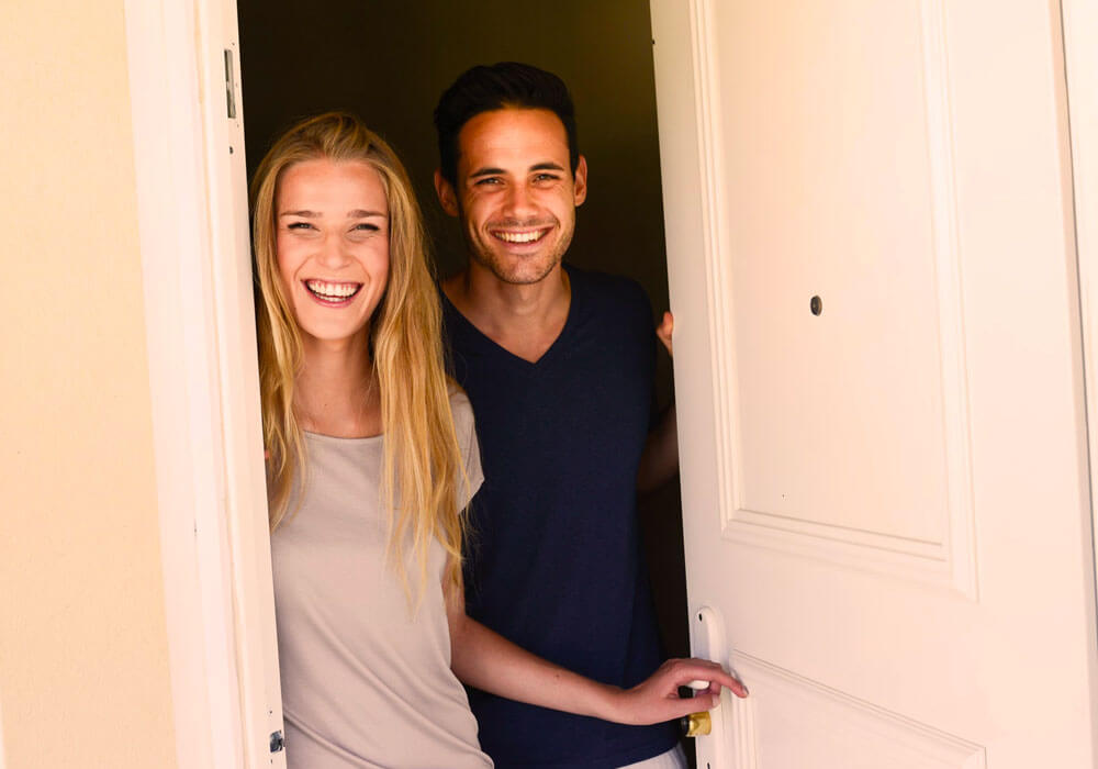 Image of a happy couple opening their apartment door as their new mattress arrives.