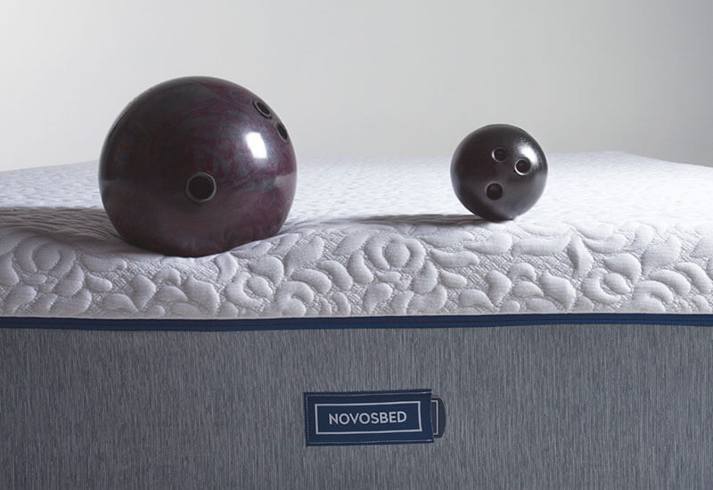 Image of a large black bowling ball and a smaller black bowling ball resting atop the front of the Novosbed premium memory foam mattress.