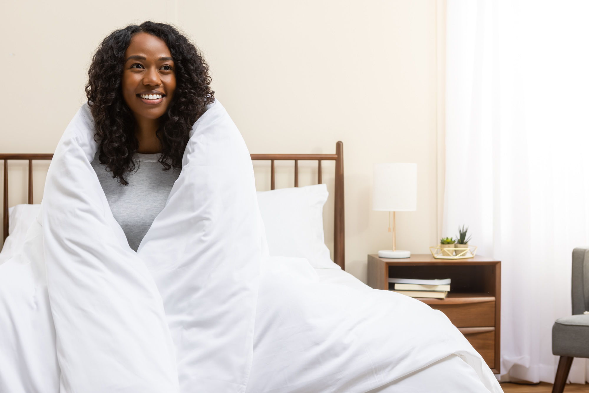 Femme souriante enveloppée dans sa couette recouverte de la housse en satin de coton