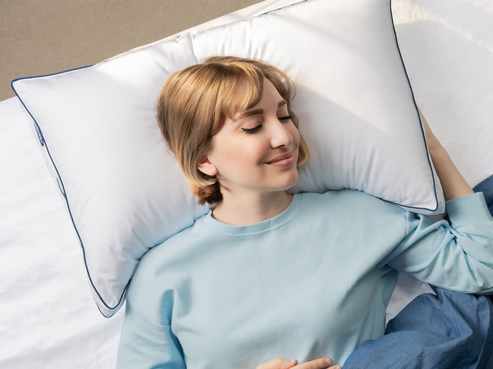 Femme joyeusement allongée dans son lit, la tête reposant sur un oreiller ajustable en mousse à mémoire de forme BonMatin.com